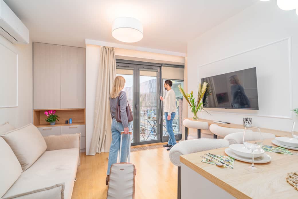 Jasny salon z aneksem kuchennym, stołem i sofą, urządzony nowocześnie w ciepłych barwach.