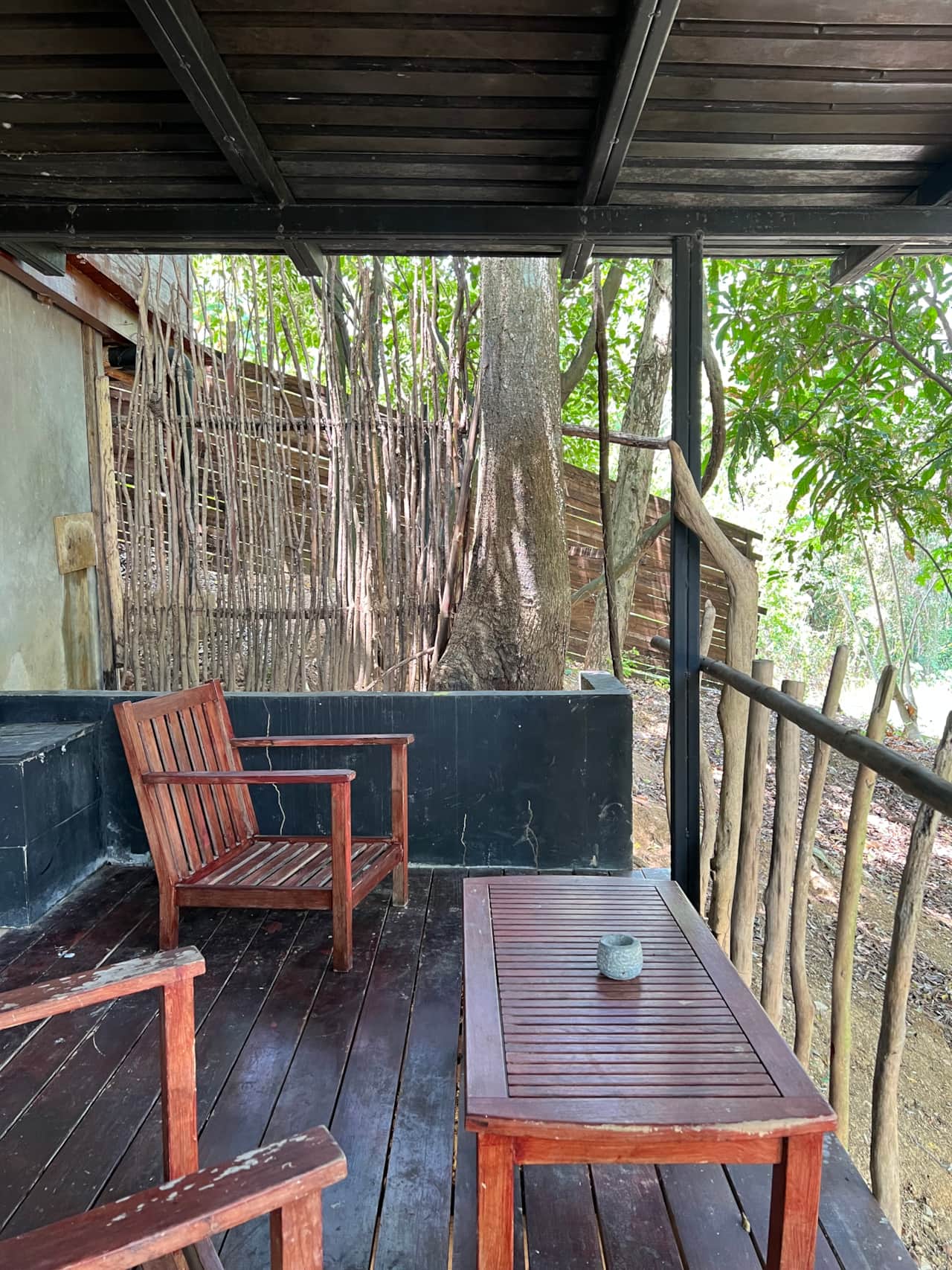 Wooden armchairs and a low table on a covered deck among the trees at Saboga Lodge