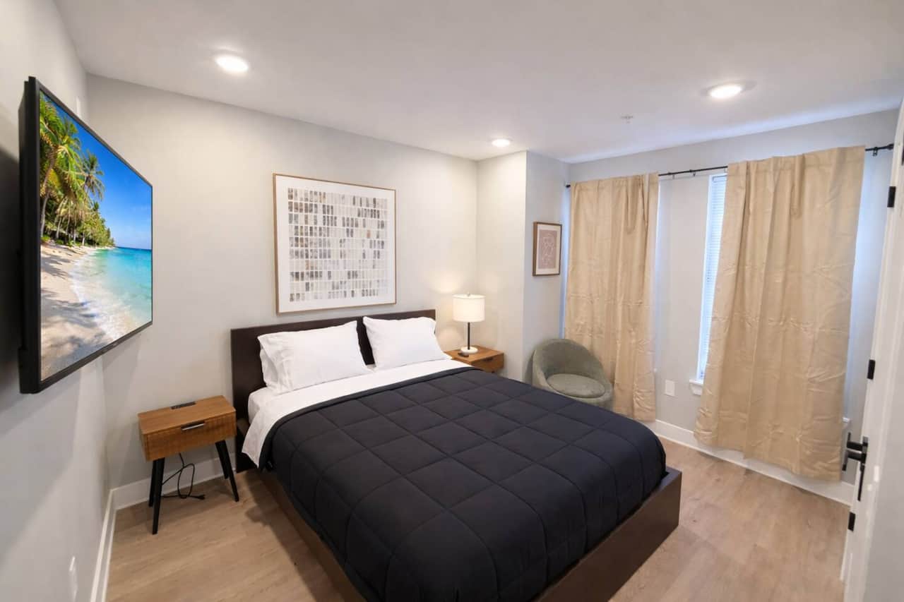 Beadeooms feature a comfortable queen-size bed with crisp white linens and a black quilted comforter. Each room includes a wall-mounted flat-screen TV, beige curtains, and a large closet.  matchingrooms are designed for a comfortable & relaxing stay!