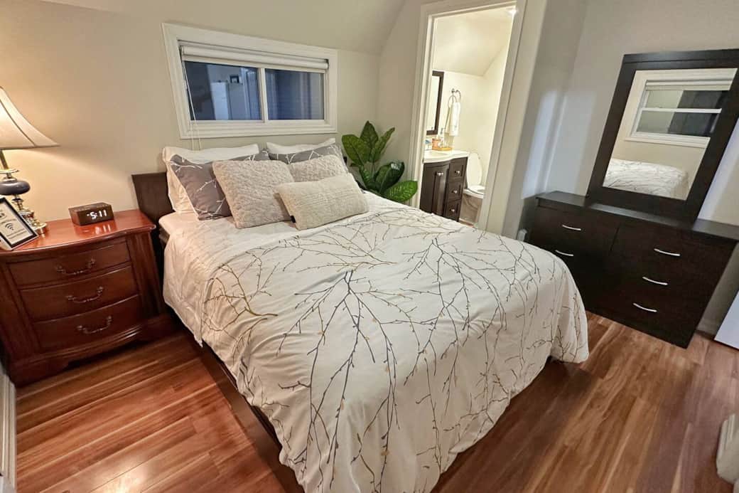 Comfortable queen bedroom with dresser, warm lighting, and convenient access to the ensuite bathroom.