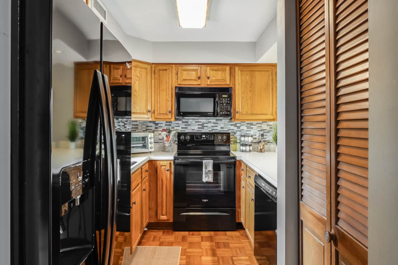 Kitchen overview with new black fridge, range, microwave, dishwasher, and oak cabinetry.  