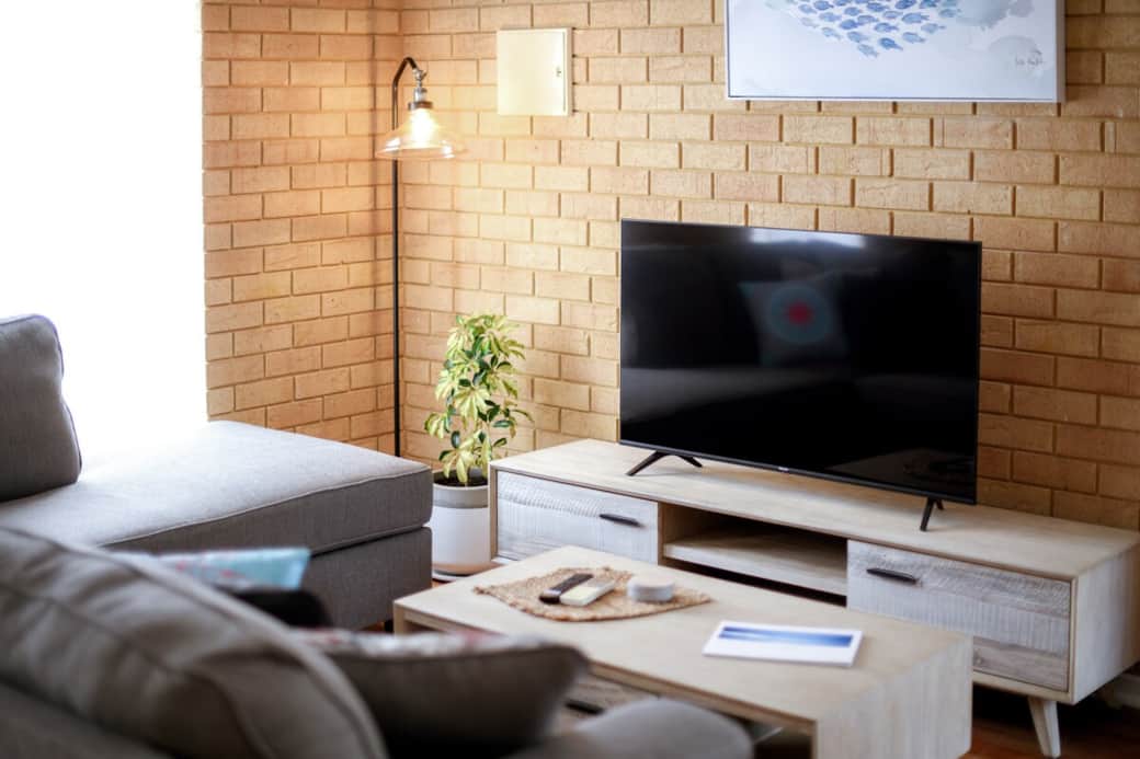 Lounge room with a comfortable couch, smart TV with Netflix and reverse cycle air conditioning unit mounted above the TV.