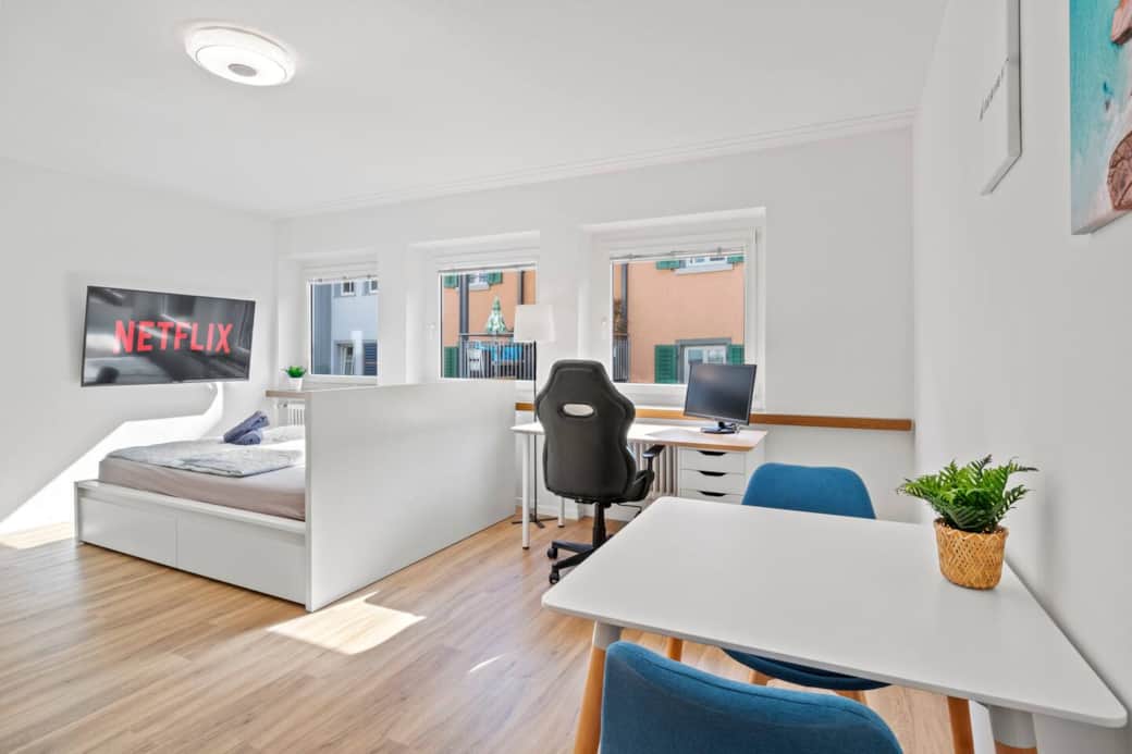 Bright studio with cozy bed, smart TV, desk and dining table.