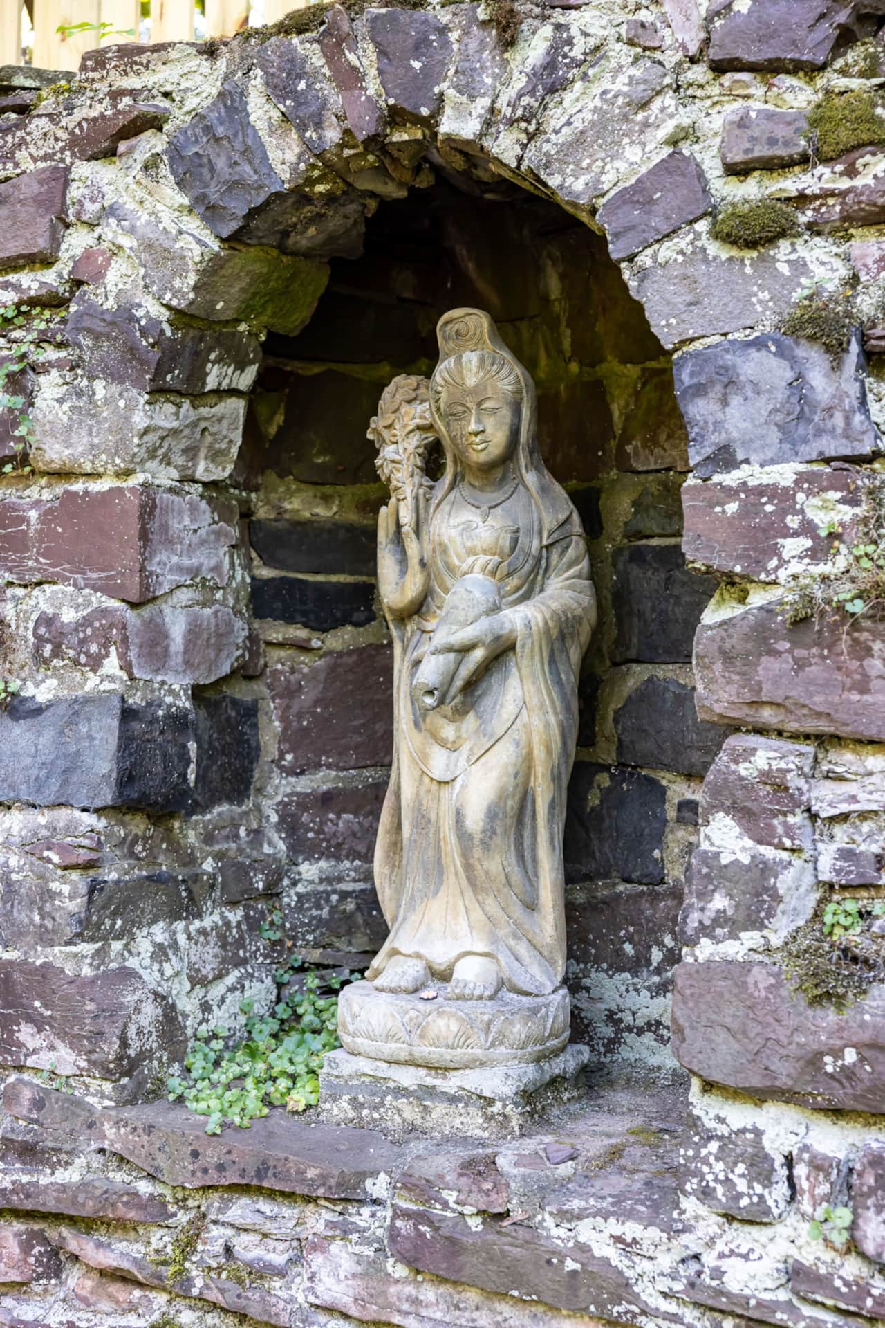 A garden statue set into an arched niche in the hand-stacked stone wall