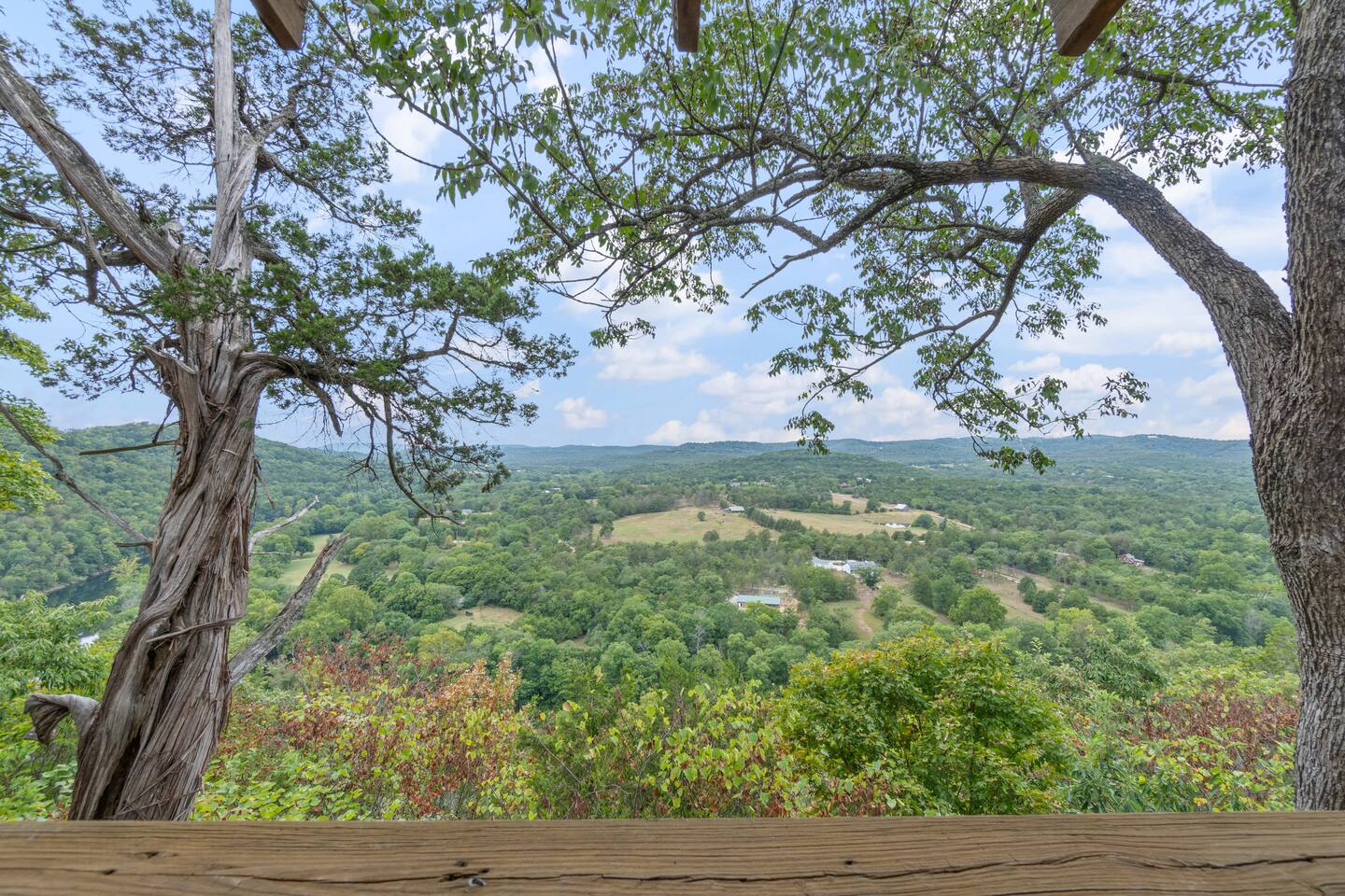 A view from a balcony or patio overlooking a lush green valley with trees and hills in the distance.