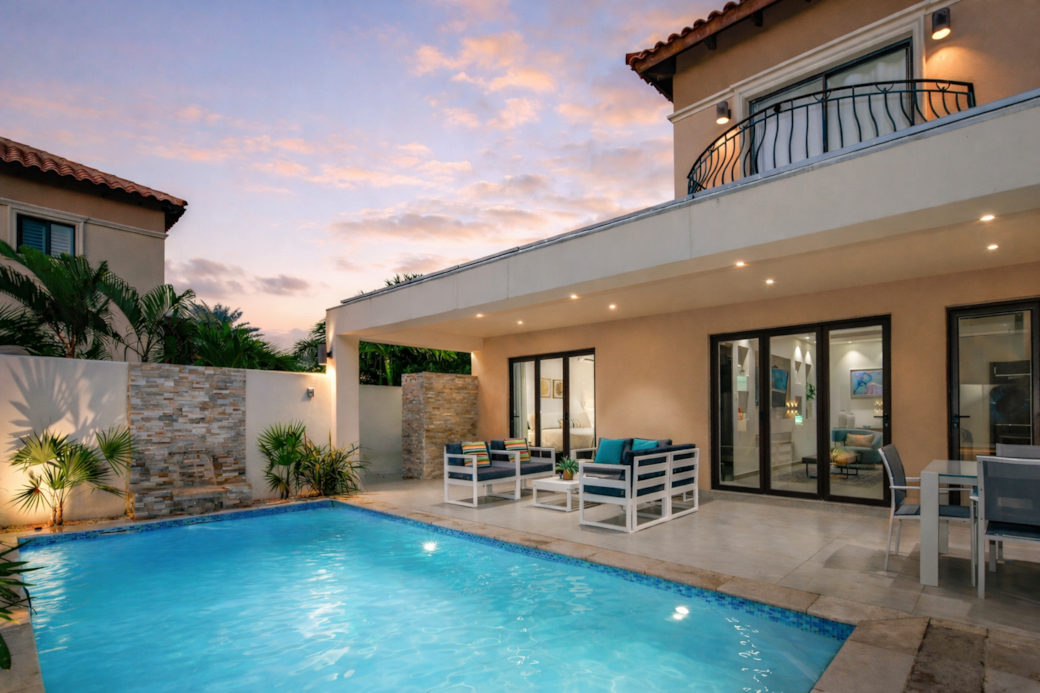 Backyard by night with pool and pagoda-covered dining table and conversation set