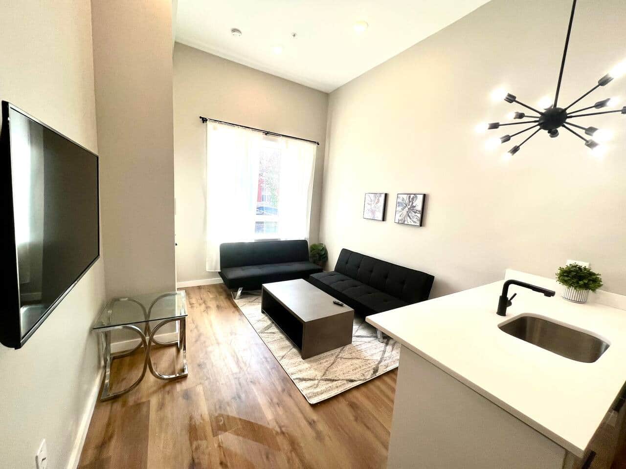 Living room with two futon sofa beds and a 50 inch TV, table connected to breakfast bar with stools and full kitchen.