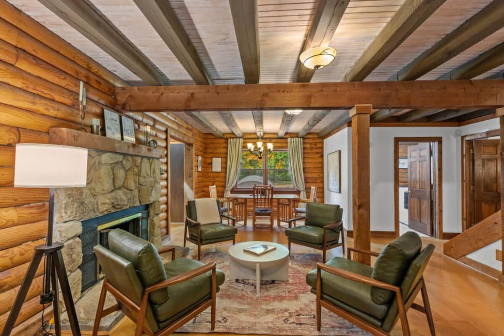 Rustic log cabin charm shines in this cozy seating area centered around a stone fireplace and exposed wood beams.