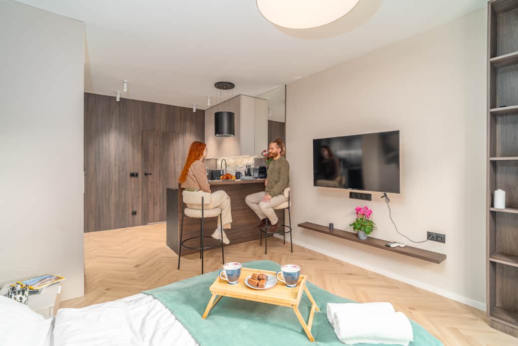 Przestronne studio z wygodnym łóżkiem, telewizorem na ścianie i funkcjonalną wyspą kuchenną.