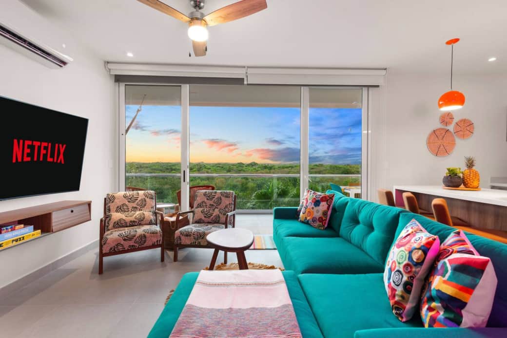 Open-concept living room with A/C and direct access to your private balcony with Akumal jungle views. Enjoy outdoor furniture and a hammock, plus books and games. Features a 65-inch smart TV and room-darkening shades.
