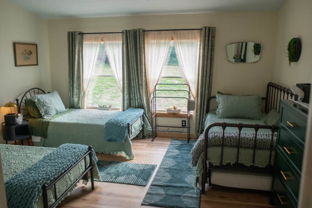 Bedroom 1, the main suite, sleeps 3–4 on eco-memory foam beds with luxurious bamboo sheets. It includes two green chests of drawers, a towel rack, a spacious walk-in closet, and touch-sensitive bedside lamps with built-in outlets.