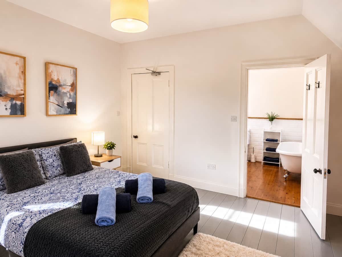 Bedroom 1 with its door open to an en-suite with a freestanding bath.