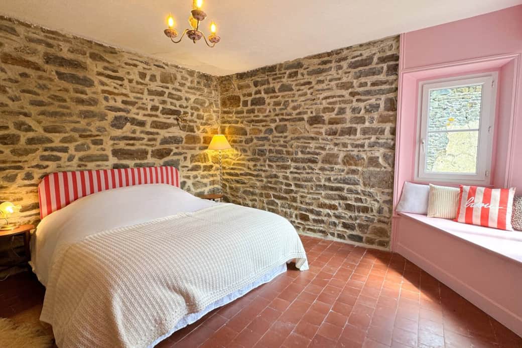 Double bedroom with exposed stone walls, bow-window and soft pink tones.