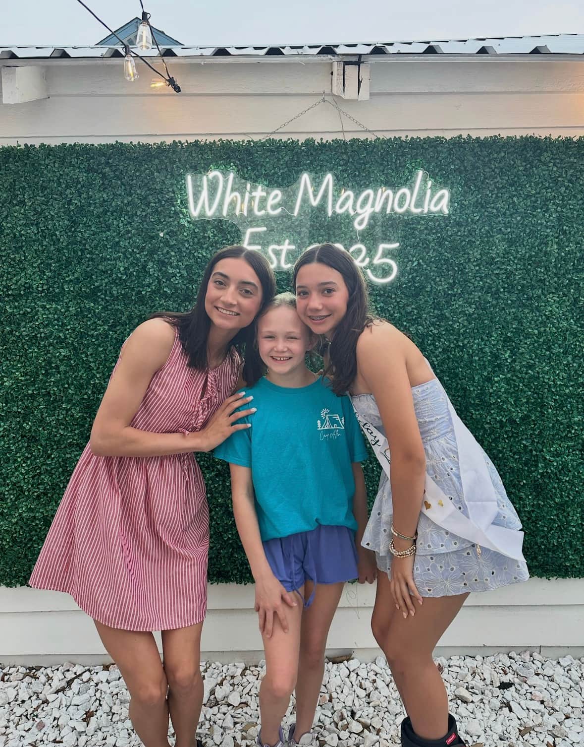 <o, and daughters in front of the photo wall of White Magnolia Galveston during their spring break vacation