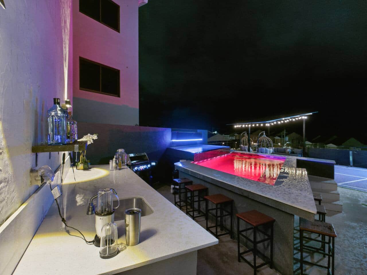 A stylish outdoor bar and lounge glows at night beside a lit pool