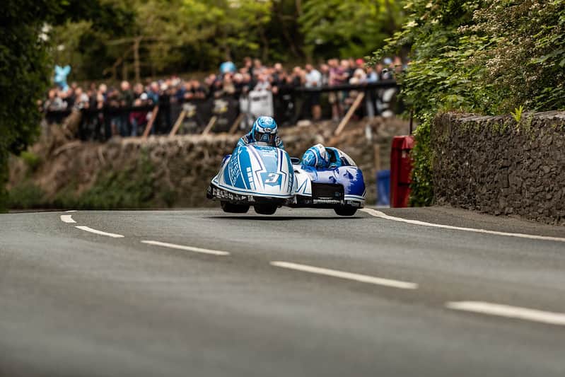 Isle of Man TT rider passing Braddan Bridge on a narrow village road (Credit Visit Isle of Man)