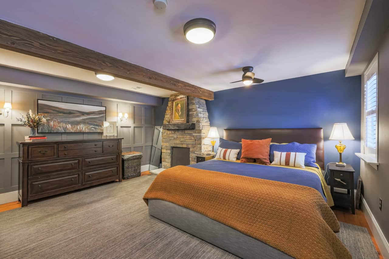 King bedroom with blue walls, a timber beam, and stone fireplace