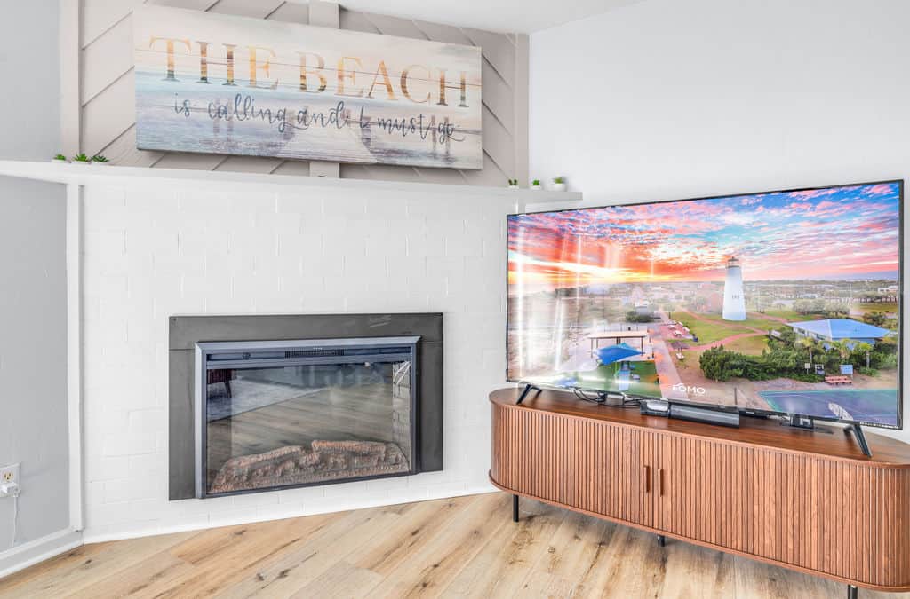 Electric fireplace with LED glow, “The beach is calling” art, and a 65” TV for cozy nights.