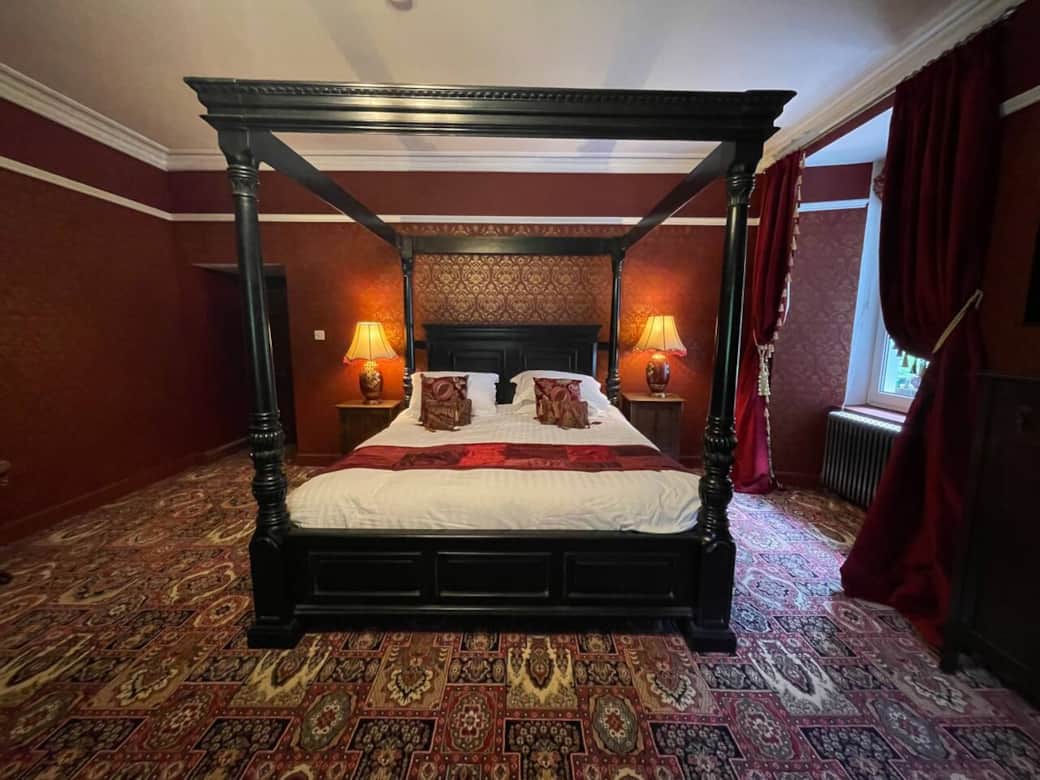 Red and gold bedroom, with super king four poster bed and En Suite. 
TV, wifi, sofa and table with tea and coffee making facilities. 
Short wardrobe with hangers, dressing table with mirror. 
