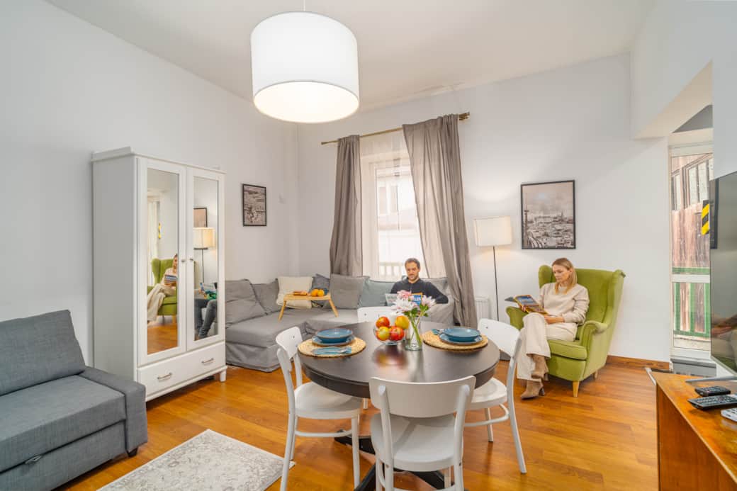 Przytulny, jasny salon z jadalnią. Wygodna szara kanapa, zielony fotel i okrągły stół .