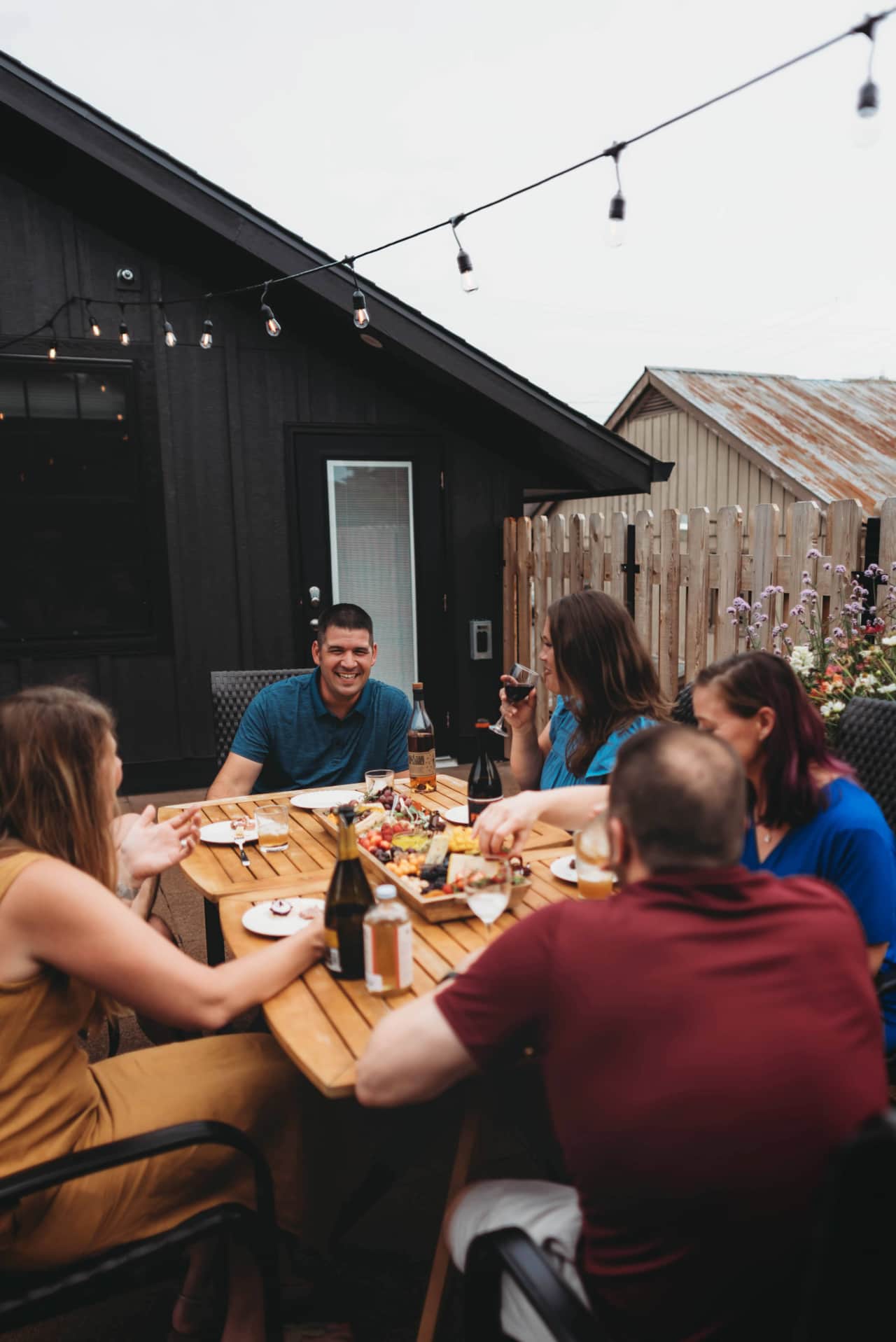A group laughs over wine and a shared meal at a long table on the rooftop patio.