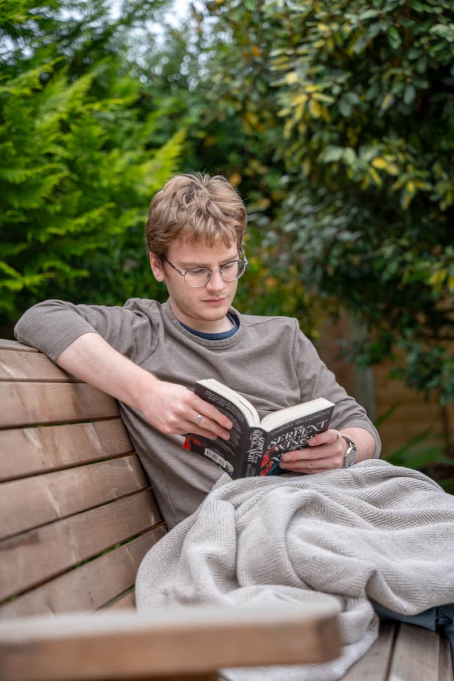 A guest reading under a blanket on a bench in the walled Secret Garden at Lonsdale House