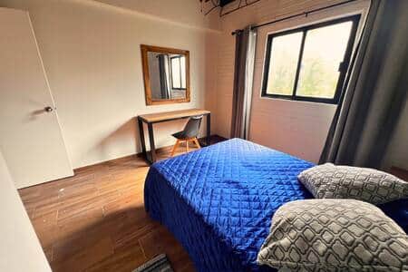 Room 8: Inviting space with soft linens, a workspace, and natural light from large windows.