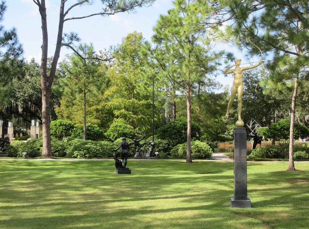 A park-like setting with several statues on a grassy area with trees and a pathway.