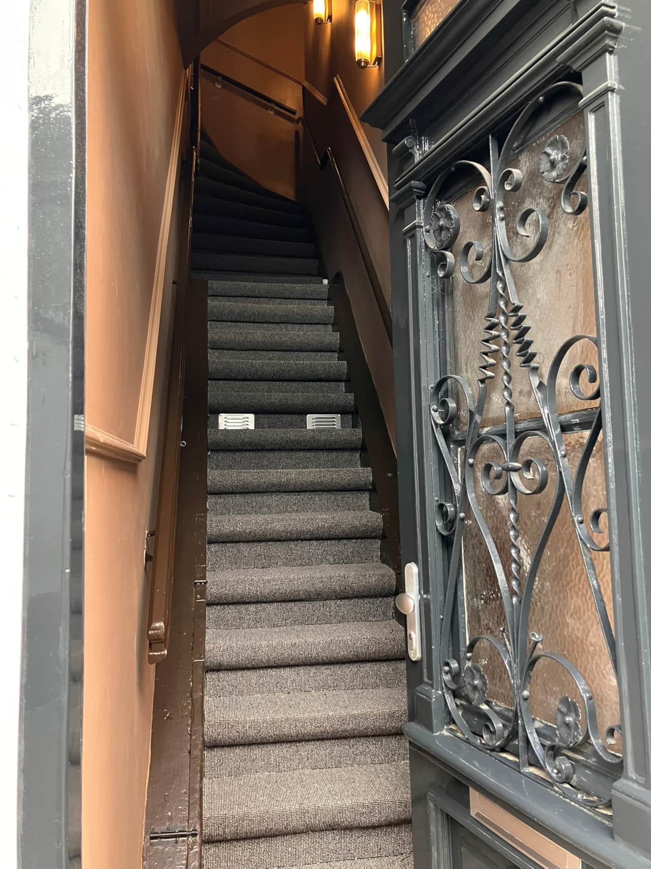 Carpeted staircase entrance of Gilded Ox Suites, with an ornate wrought-iron gate
