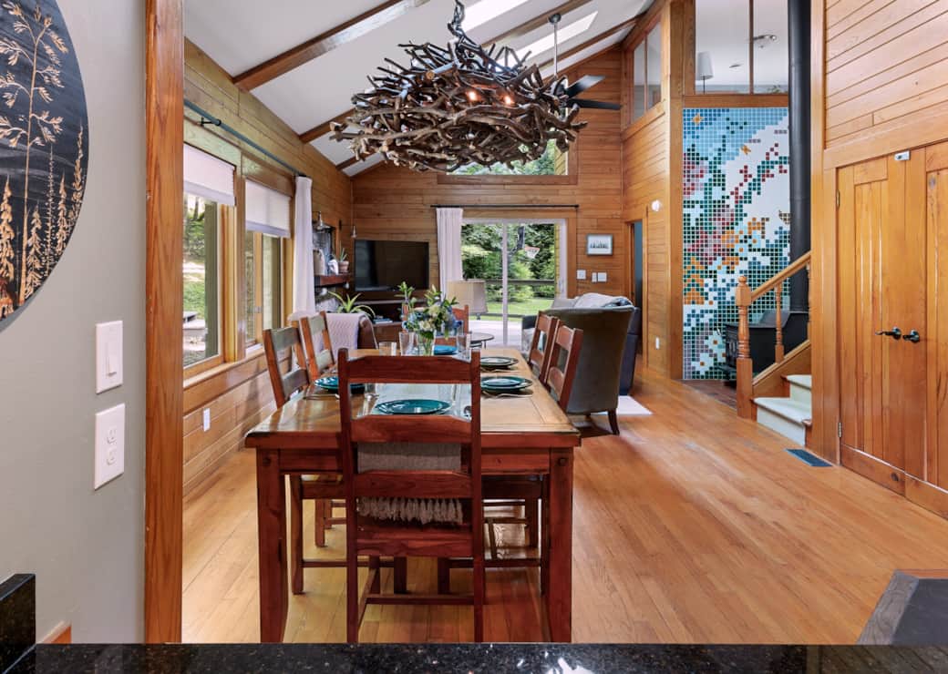 View from kitchen with dining for 6, wood stove on mosaic wall, and light from skylights & doors.