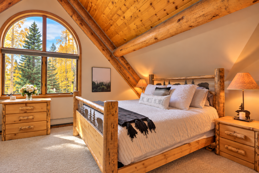 Log bed under a vaulted pine ceiling with an arched window onto fall aspens