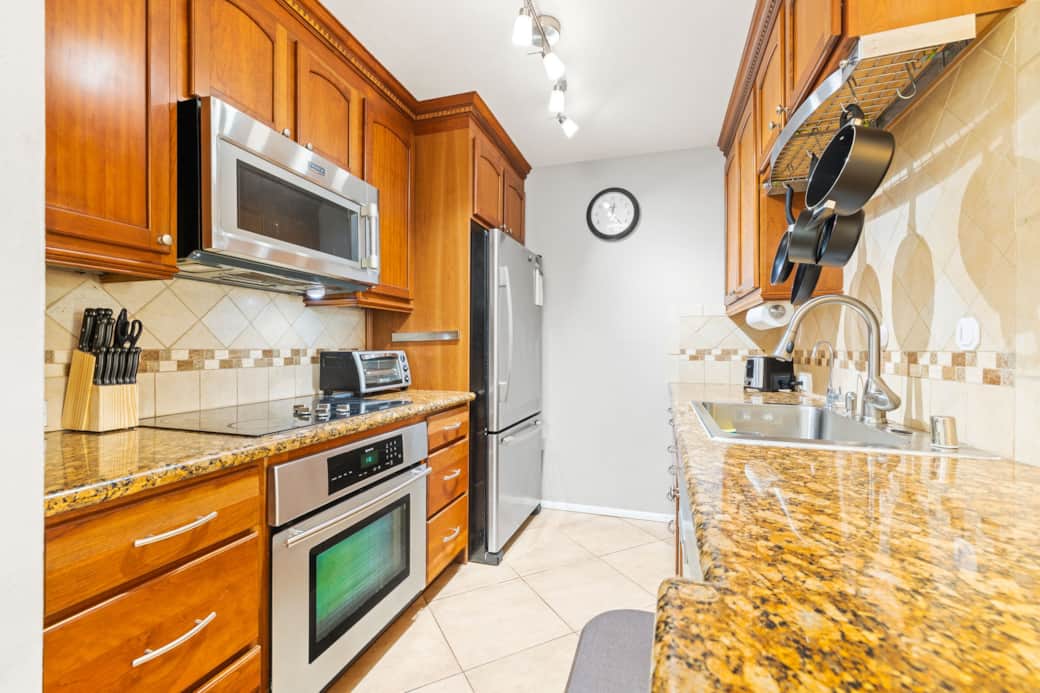Warm, fully equipped galley kitchen with granite countertops and stainless steel appliances.