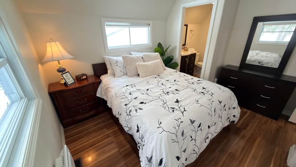 Comfortable queen bedroom with dresser, warm lighting, and convenient access to the ensuite bathroom