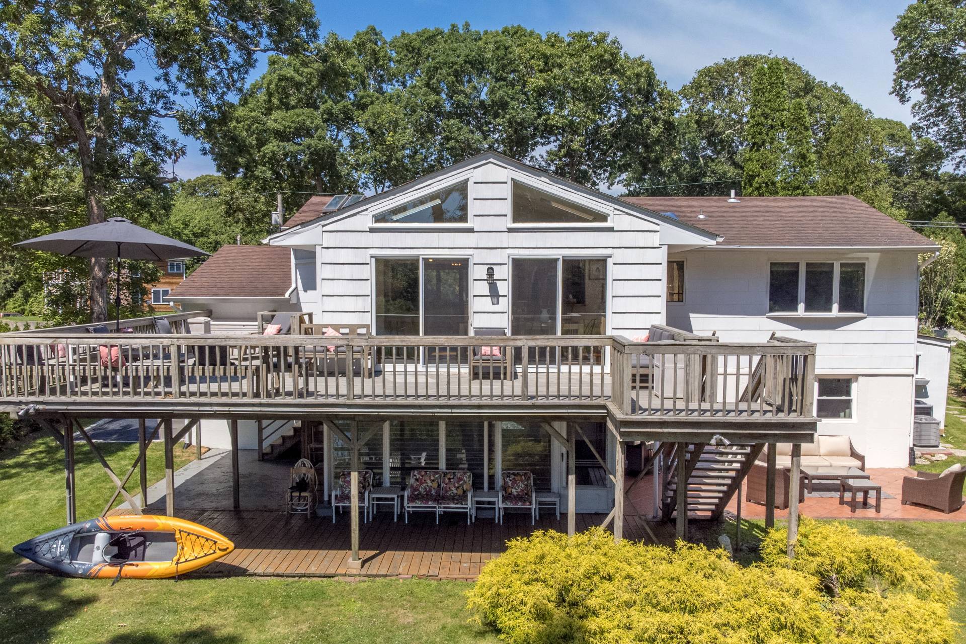 Back of the house with the oversized deck, lower patio and a kayak