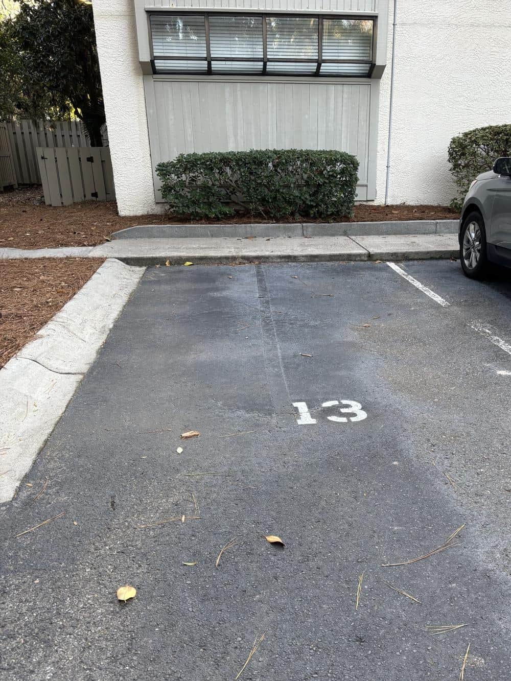 Parking space 13 at Springwood Villas, marked with a painted 13, with a low curb and a level concrete walkway along the front of the building