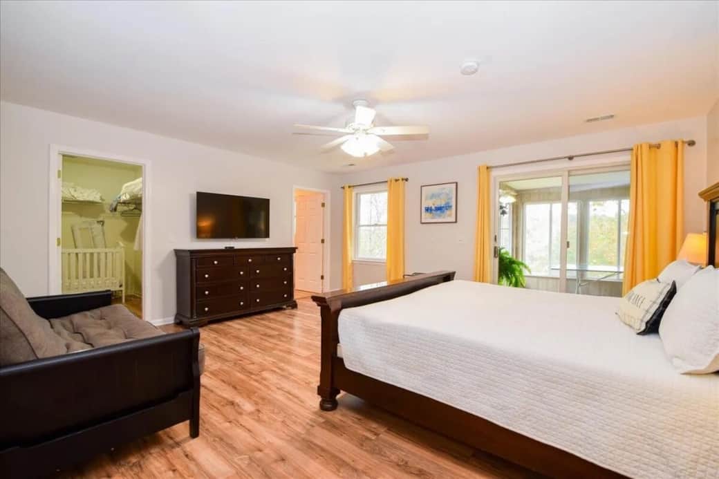 Spacious primary king suite with walk-in closet, flat-screen TV, and private sunroom access overlooking the lake.ing bed, walk-in closet, primary suite, sunroom access, flat-screen TV, luxury LVP floors, natural light, lake house master bedroom.