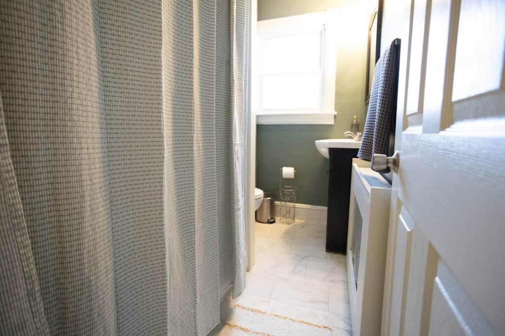 A fresh, inviting bathroom featuring soft green walls, bright natural light, and a clean, minimalist design. Stocked with essentials for a comfortable stay.