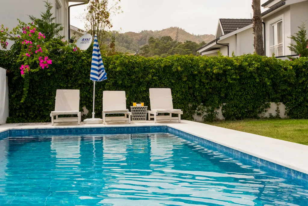 Swimming pool with sun loungers and an umbrella, surrounded by greenery at Villa Nergis 3, Gocek.