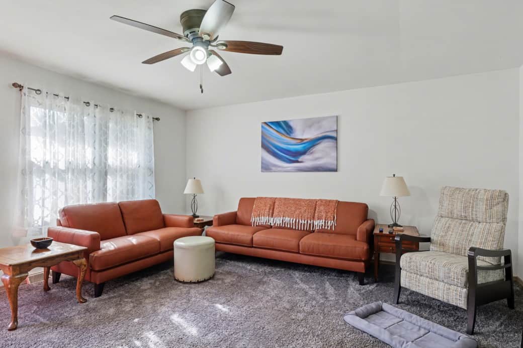 Living room with seating for 6, a recliner and a large Roku TV. Hallway to the bedroom on the right.