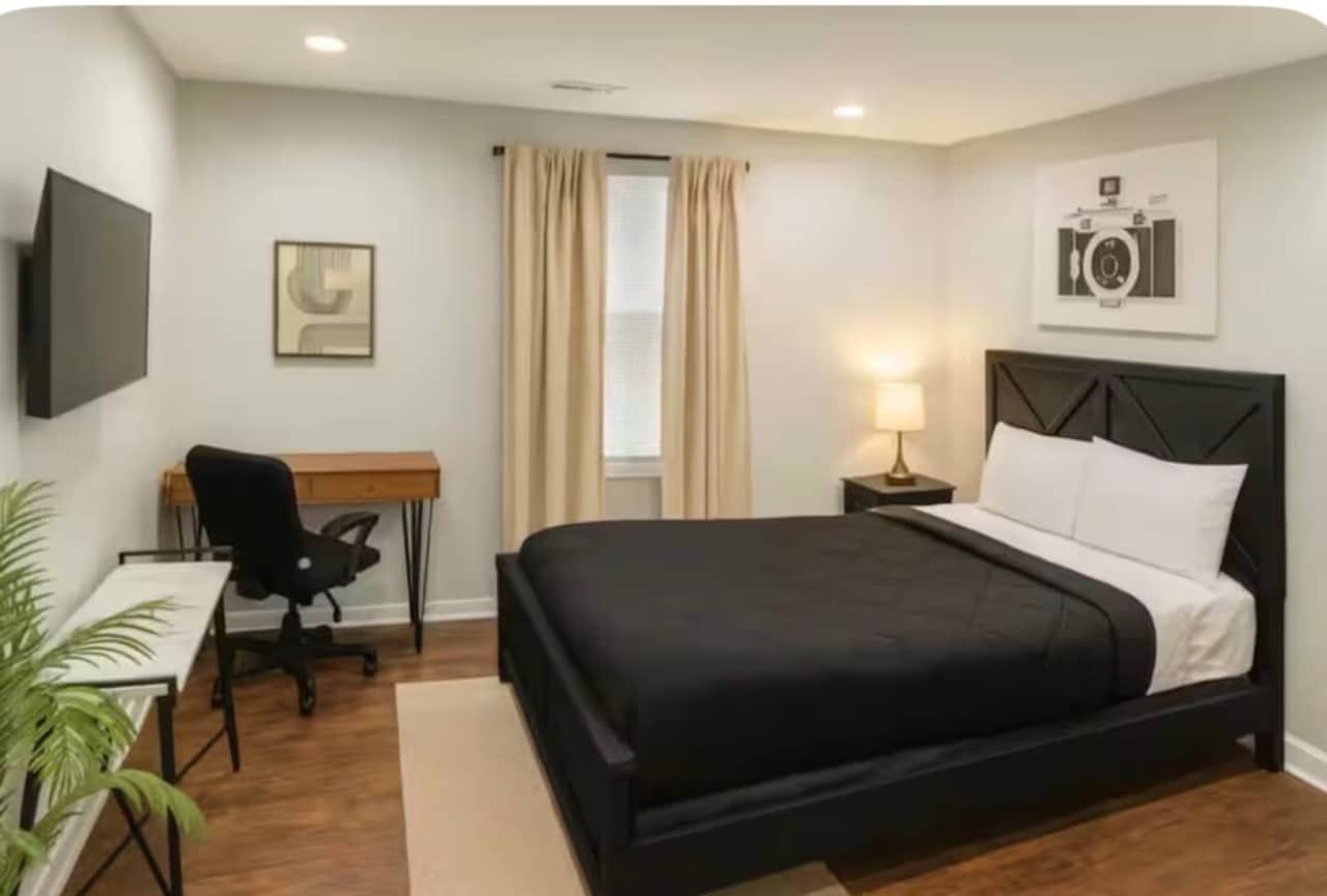 Queen bed with work desk, flatscreen TV and blackout curtain curtains.