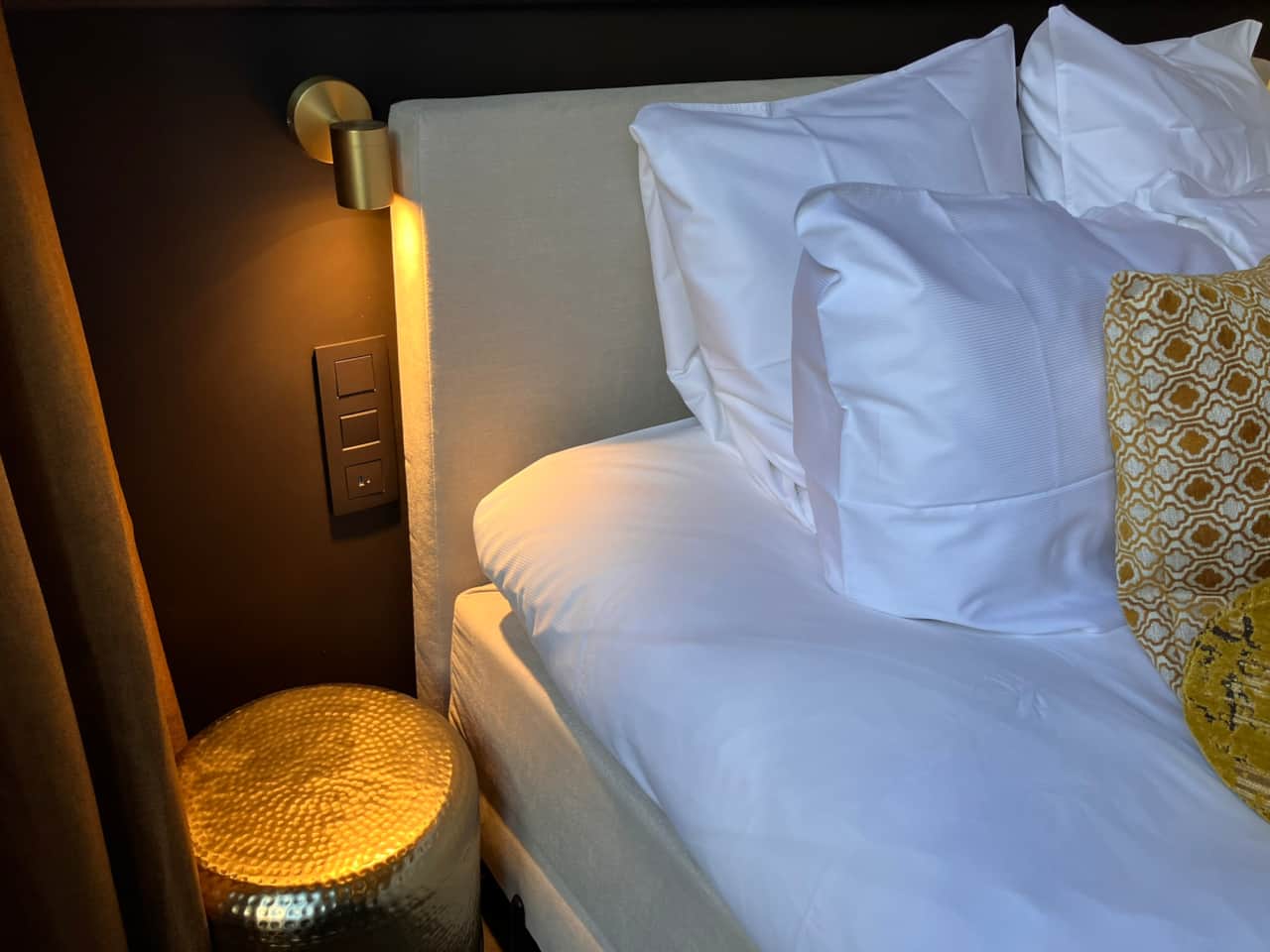 Close-up of the Aleida Suite bed, mustard bolster and pillows against the headboard and wallpaper mu