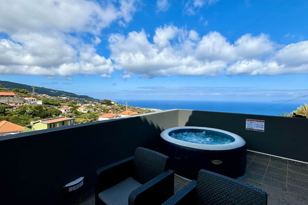 A picturesque terrace with a hot tub and seating area, offering a daytime view of a coastal town and the ocean under a partly cloudy sky. A picturesque terrace with a hot tub and seating area, offering a daytime view of a coastal town and the ocean under a partly cloudy sky.