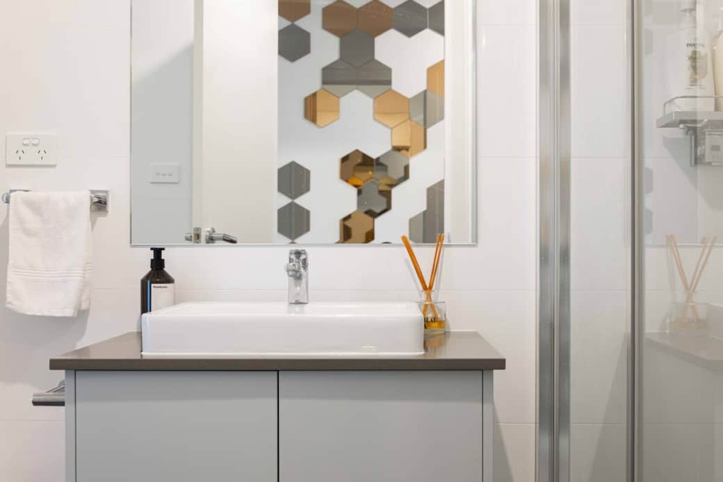 Step into a bathroom with modern elegance. The sleek sink, stylish faucet, and large mirror create a sophisticated ambiance. The glass shower enclosure adds to the spacious feel, while the white tiles and countertop offer a timeless appeal. 