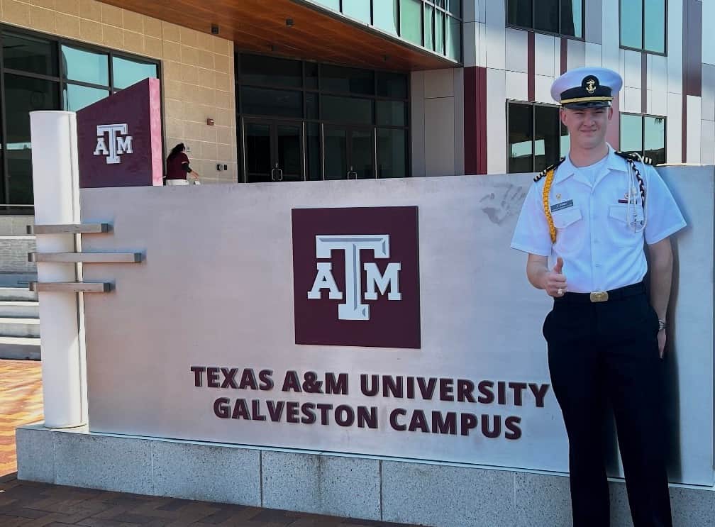 Texas A&M Galveston graduate celebrating outside campus sign during graduation weekend