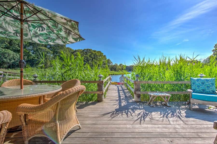 Dining table under an umbrella on the dock, with beach grass and the cove beyond