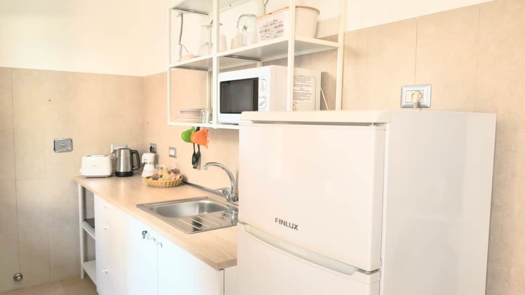 Angolo cottura con frigo, microonde, tostapane, bollitore, macchina del caffè, stoviglie.