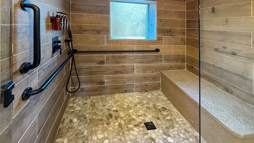 Elegant bathroom with zero-entry walk-in shower featuring built-in bench and handheld sprayer