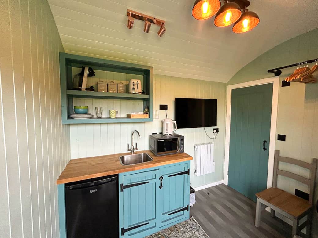 Compact kitchenette with pastel cabinetry, dining essentials and cosy rustic touches.
