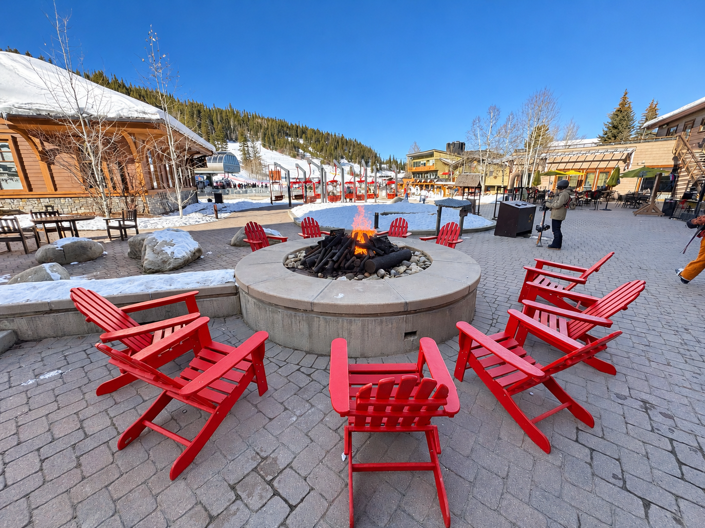 Snowy Winter Park Resort village with red chairs around a firepit