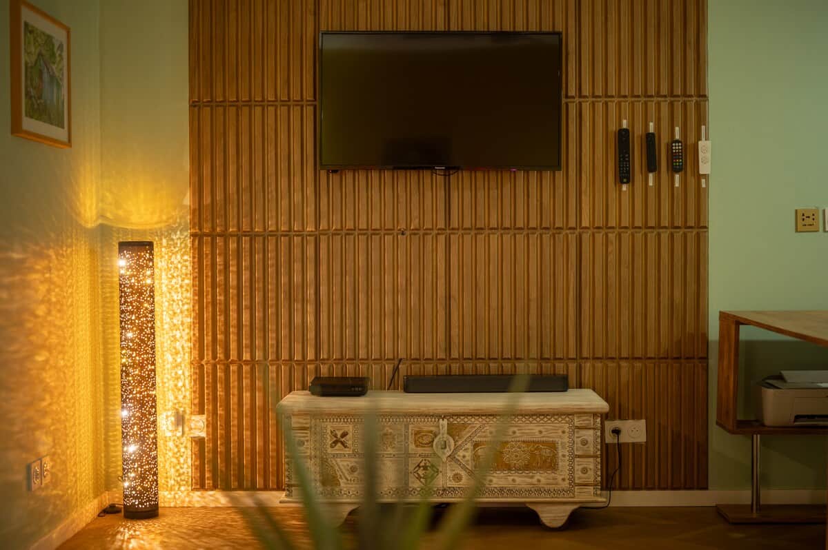 Salon avec TV, murs verts, panneaux en bois et éclairage d'ambiance